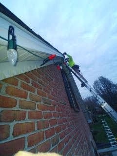 E.L.F. Designs technician clipping Christmas lights to a roofline gutter on a brick home in Abingdon, Maryland