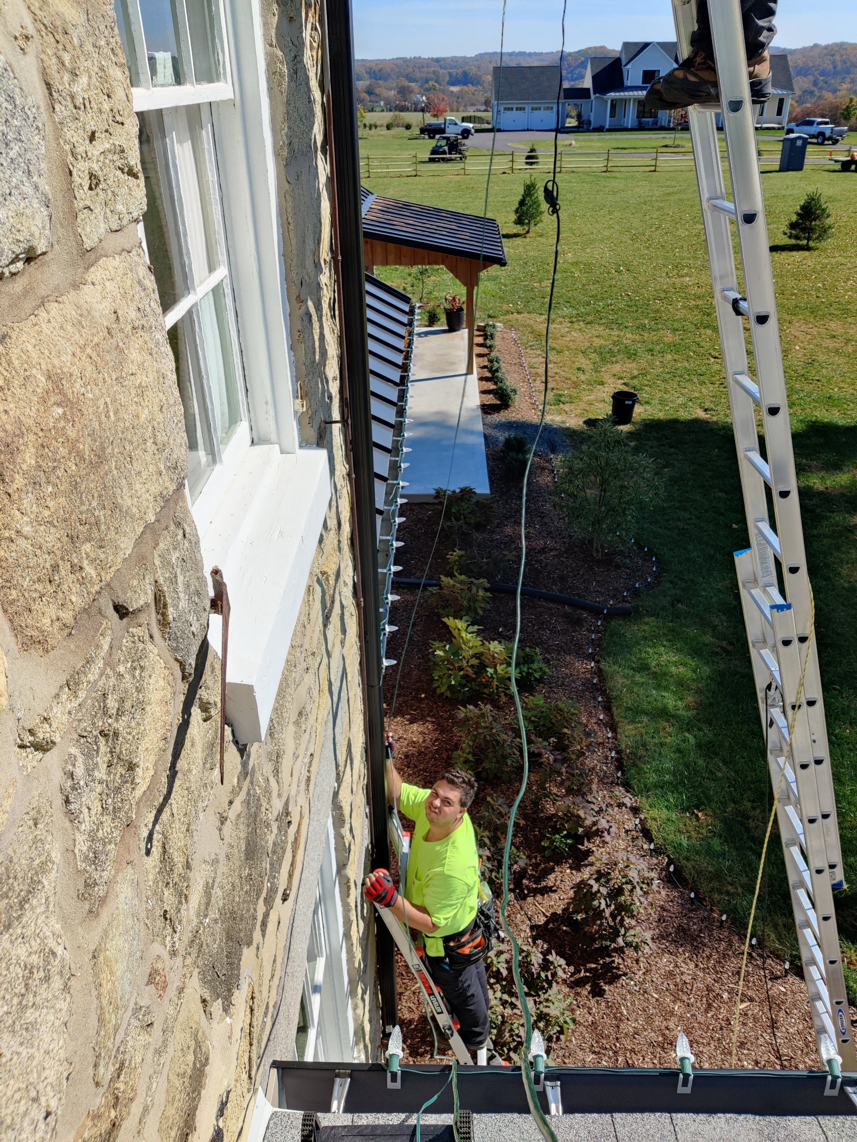 E.L.F. Designs crew member on a ladder installing holiday lights on a stone home in Bel Air, Maryland