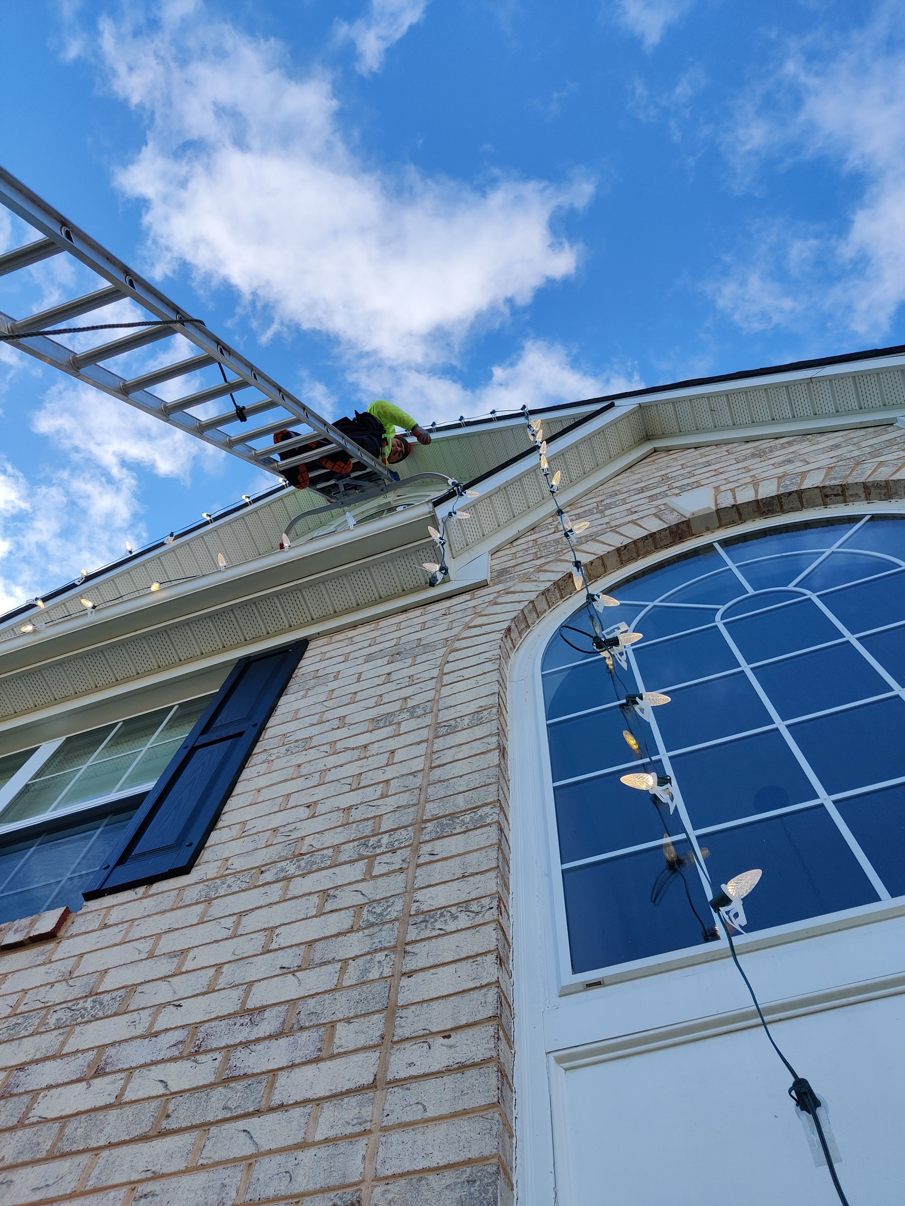 E.L.F. Designs technician on a ladder installing Christmas lights on a brick home in Fallston, Maryland