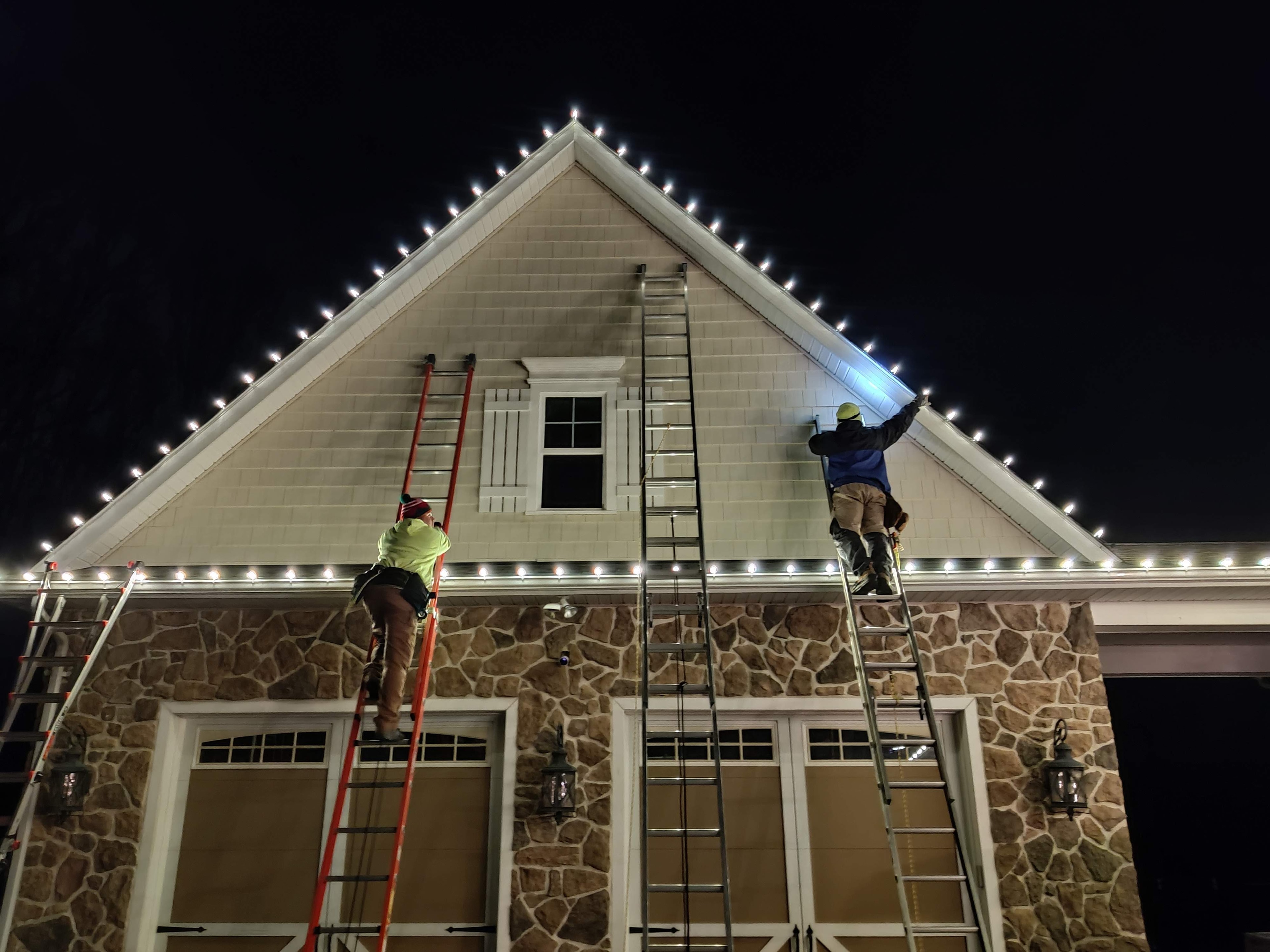 E.L.F. Designs crew on ladders installing holiday lights on a stone home at night in Abingdon, Maryland