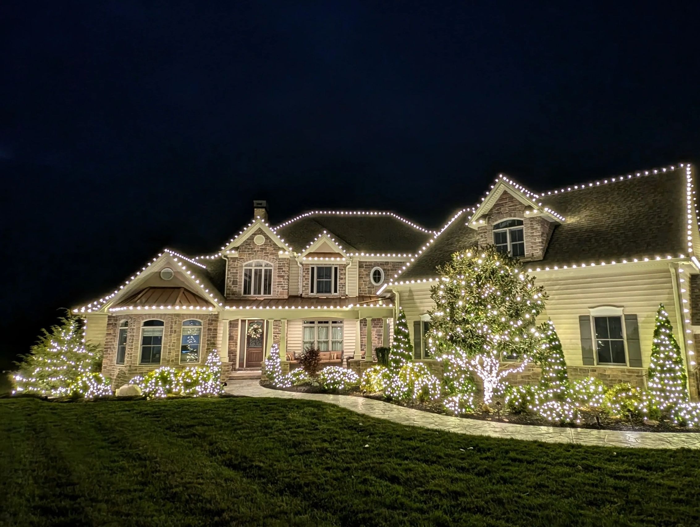 Warm white lights outline rooflines and landscape greenery at night.